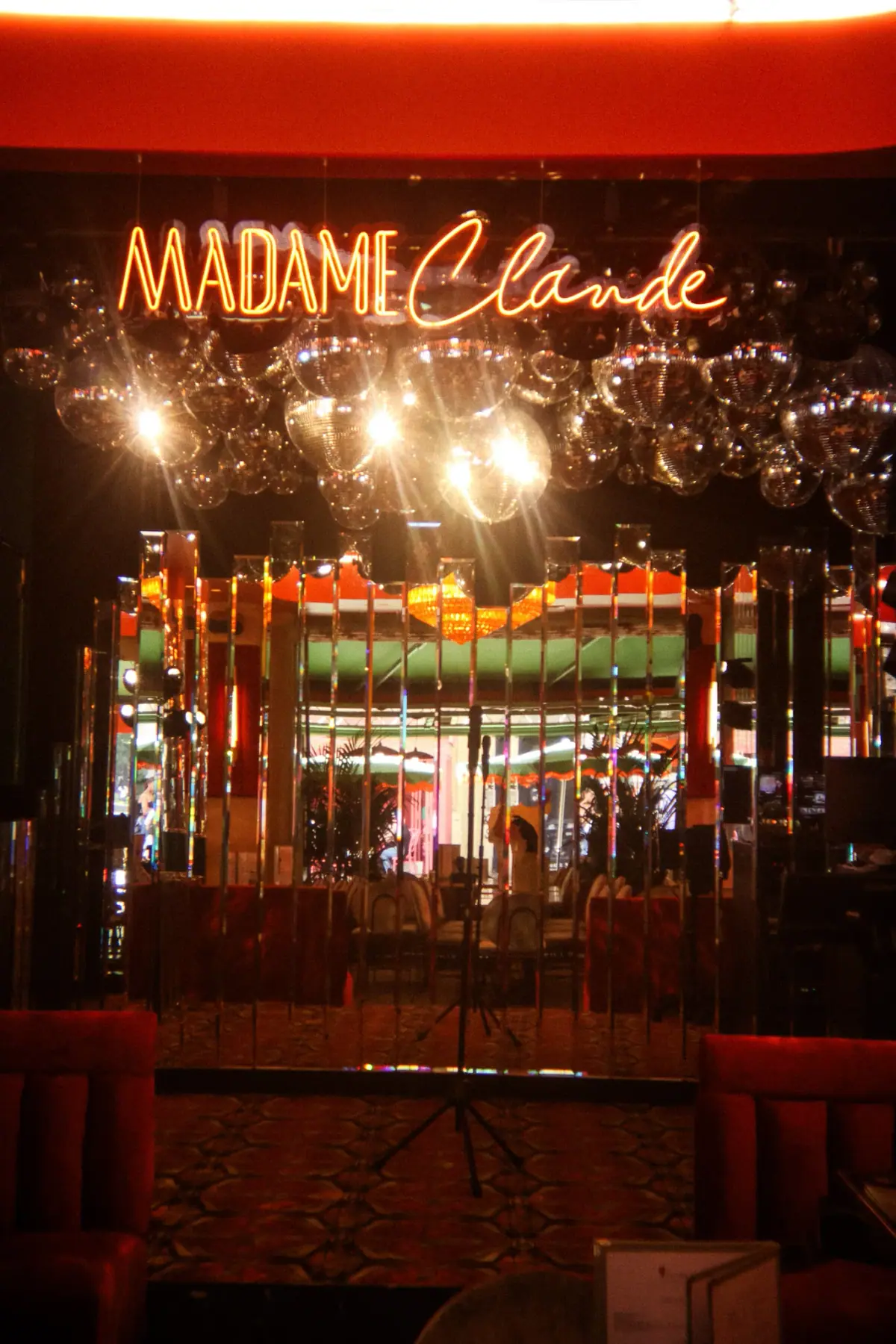 Enseigne néon rétro Madame Claude illuminant la scène de karaoké, restaurant années 70 à Paris