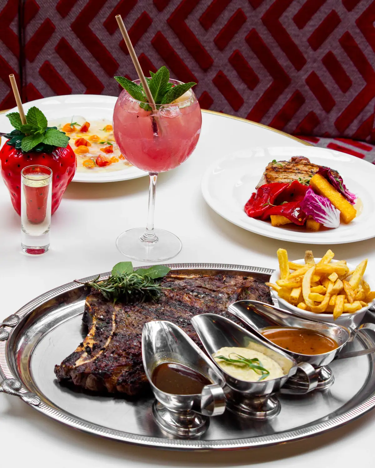 Grande côte de bœuf à partager, servie avec frites, sauces et cocktails pour un repas convivial.
