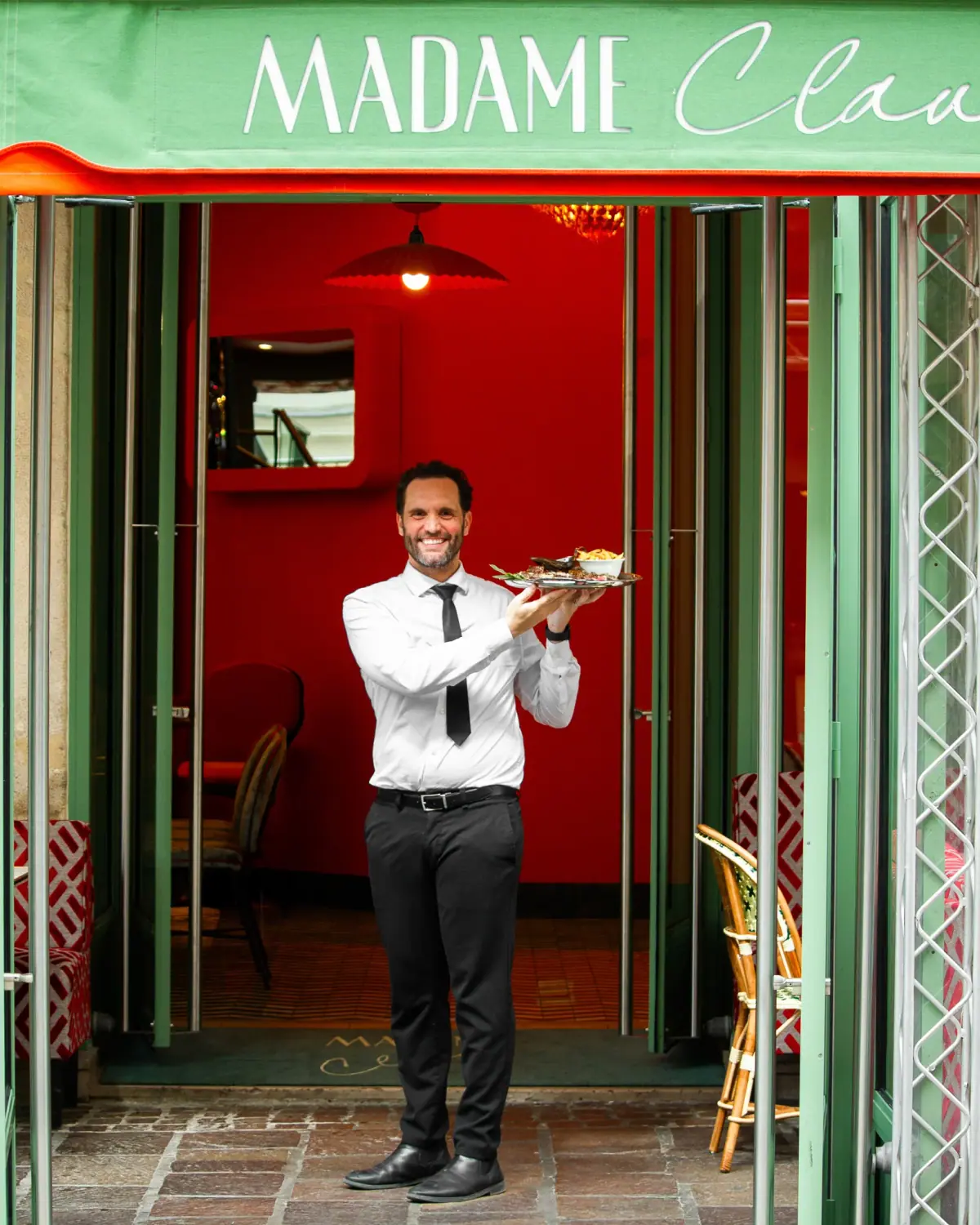 Un serveur souriant du Madame Claude présentant une sélection de plats du jour.