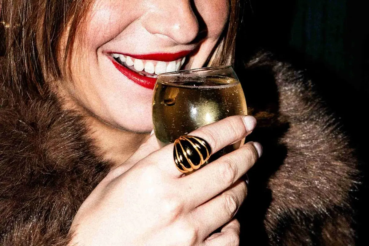 Invitée souriante, un verre à la main, au réveillon du Nouvel An de Madame Claude
